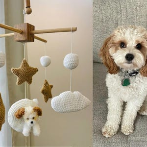 May include: A white and brown crocheted baby mobile with a cloud, stars, and a small dog hanging from a wooden frame.
