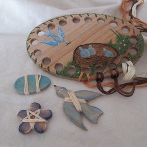 May include: A wooden bird themed embroidery floss organizer with 18 holes. The organizer is painted with blue birds, a nest with three baby birds, and green leaves. There are three additional wooden bird shapes with string wrapped around them.