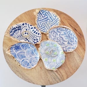 May include: Five blue and white patterned oyster shell ring dishes with gold accents on a wooden tray. Two rings are visible in one of the dishes.
