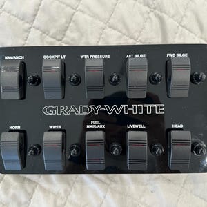 May include: A black control panel with ten rocker switches. The panel has white text that reads "GRADY-WHITE" and labels for each switch, including "NAV/ANCH", "COCKPIT LT", "WTR PRESSURE", and "HORN".