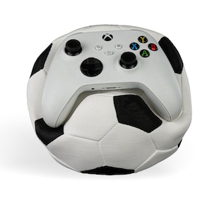 Op de afbeelding: Een witte Xbox-controller die op een witte en zwarte voetbal ligt.