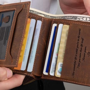 May include: A brown leather wallet with a personalized inscription that reads "How wonderful life is while you're in the world. I love you more than life itself. Forever yours, Liz". The wallet has multiple card slots and a clear ID window.
