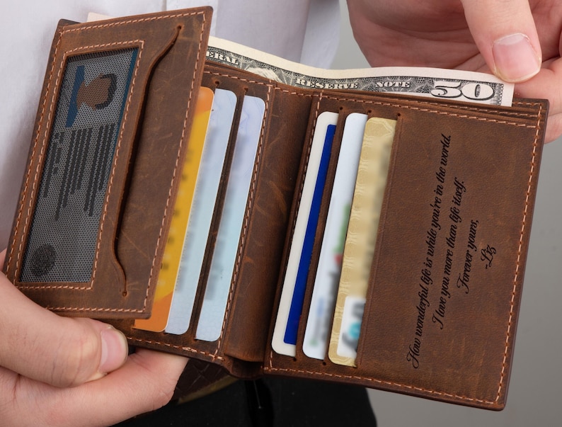 May include: A brown leather wallet with a personalized inscription that reads "How wonderful life is while you're in the world. I love you more than life itself. Forever yours, Liz". The wallet has multiple card slots and a clear ID window.