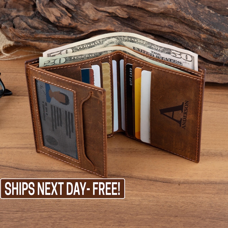 May include: A brown leather wallet with multiple card slots and a clear ID window. The wallet is open and has a personalized initial "A" and the name "Anderson" engraved on the outside.