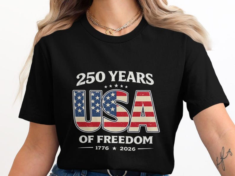 May include: Black t-shirt with a patriotic design celebrating 250 years of American freedom. The design features the text "250 YEARS USA OF FREEDOM 1776-2026" in white, red, and blue, with the USA letters incorporating the American flag.