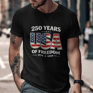 May include: Black t-shirt with a patriotic design. The shirt features the text "250 YEARS USA OF FREEDOM 1776-2026" in white and red, with the USA letters designed as the American flag. The shirt is a classic crew neck.