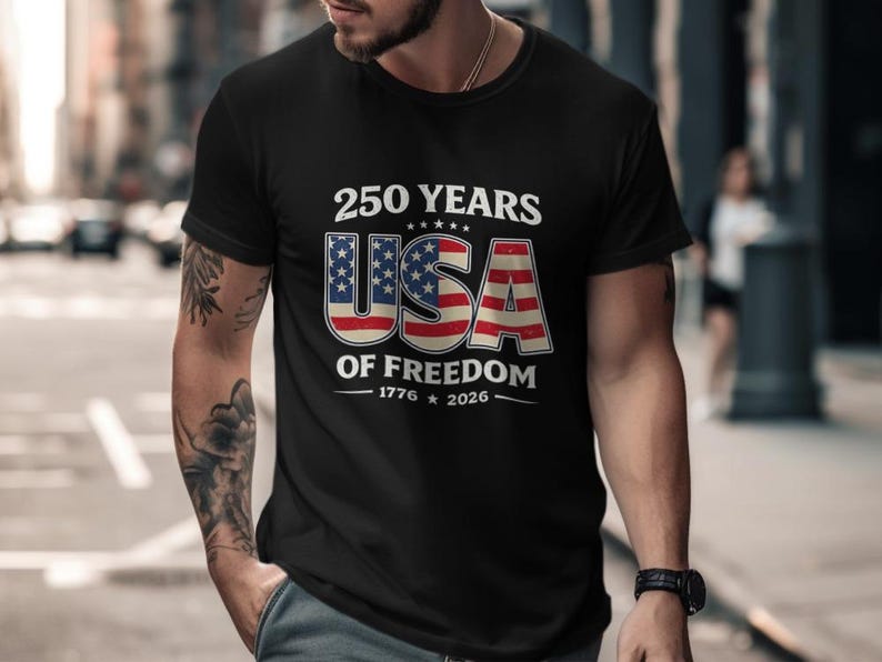 May include: Black t-shirt with a patriotic design. The shirt features the text "250 YEARS USA OF FREEDOM 1776-2026" in white and red, with the USA letters designed as the American flag. The shirt is a classic crew neck.