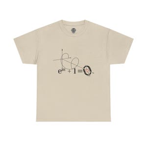 Op de afbeelding: Een beige t-shirt met korte mouwen en een zwarte grafische print van de wiskundige vergelijking e^iπ + 1 = 0. De nul is afgebeeld als een doelwit met een klein rood hartje in het midden, doorboord door een pijl, met een coördinaatas erboven.