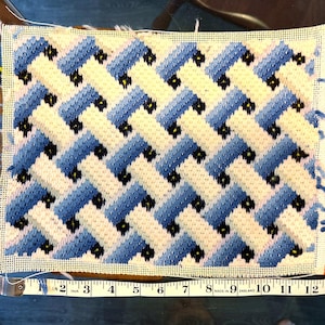 May include: A blue and white needlepoint canvas with a geometric pattern of blue and white squares and black dots. The canvas is 12 inches wide.