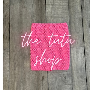 May include: A vibrant pink crochet fabric square with the text "the tutu shop" in a cursive font. The fabric is a solid colour and appears to be stretchy. The background is a wooden surface.