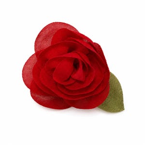 Può includere: Una spilla a forma di rosa in tessuto di colore rosso vivace con petali stratificati e semitrasparenti disposti in un motivo floreale circolare. Una singola foglia testurizzata verde oliva è attaccata al lato inferiore destro del fiore.
