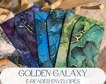 Puede incluir: Una colección de cinco fundas rectangulares para lectores electrónicos con un patrón de mármol abstracto en tonos gris, morado, azul, verde azulado y verde, acentuadas con vetas y motas doradas. El texto dice GOLDEN GALAXY E-READER ENVELOPES.