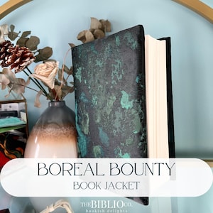 Peut inclure: Un livre relié avec une couverture en tissu texturé noir et bleu sarcelle chiné. Le livre est placé debout, montrant ses pages blanches. Le texte BOREAL BOUNTY BOOK JACKET est imprimé en lettres bleu foncé au bas de l'image.