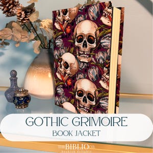 Peut inclure: Un livre à couverture rigide avec une jaquette violet foncé ornée d'un motif répétitif de crânes humains et de tulipes. Les crânes présentent des ombrages détaillés et les pages sont de couleur crème. Le texte GOTHIC GRIMOIRE BOOK JACKET est visible.