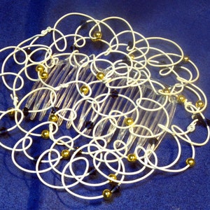 May include: A white wire hair comb with gold and black beads. The comb is decorated with a swirling pattern of wire.