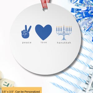 May include: A white, round ornament with a red ribbon for hanging. The ornament features blue graphics of a peace sign, a heart, and a menorah, with the words "peace", "love", and "hanukkah" below. The ornament measures 3.5" x 3.5" and can be personalized.