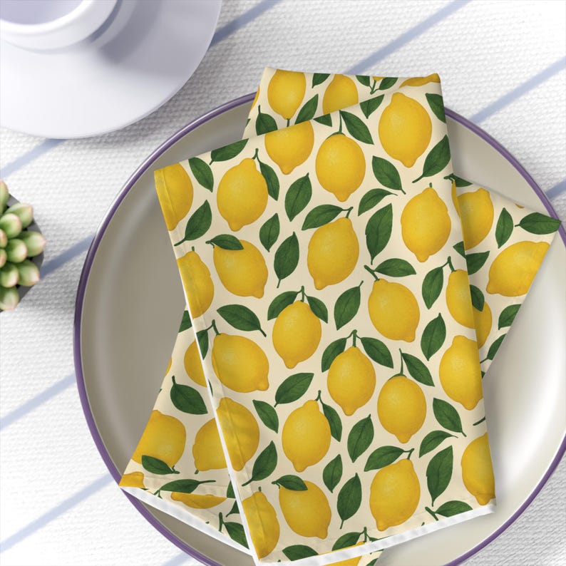 Image is of printed Mediterranean citrus yellow lemon napkins on a plate on a striped tablecloth view