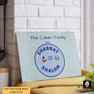 May include: A blue and white cutting board with the text "The Cohen Family 2025" and a blue circle with the text "Shabbat Shalom" and a Star of David, wine bottle, and candles inside.