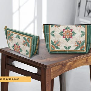 K&ouml;nnte beinhalten: Zwei dekorative Beutel mit floralen Mustern. Die Beutel haben einen cremefarbenen Hintergrund mit einem sich wiederholenden Design aus Blumen und Bl&auml;ttern in Orange-, Rosa- und Gr&uuml;nt&ouml;nen. Die R&auml;nder sind mit gr&uuml;nen und goldenen Akzenten versehen. Sie werden auf einem Holztisch ausgestellt.