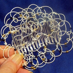 May include: White wire hair comb with gold and black beads. The comb is in the shape of a flower.