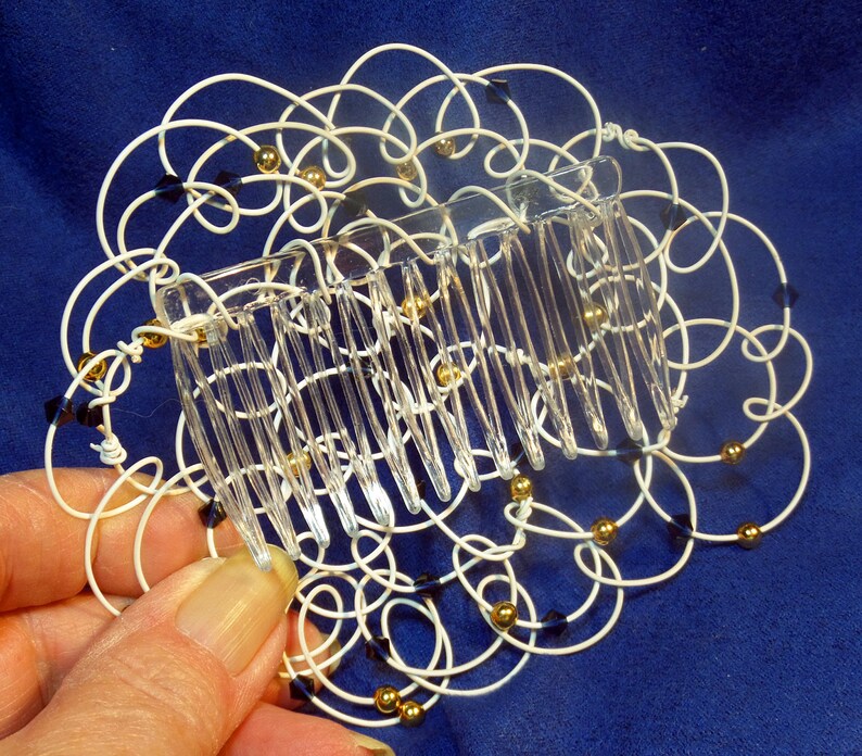May include: White wire hair comb with gold and black beads. The comb is in the shape of a flower.