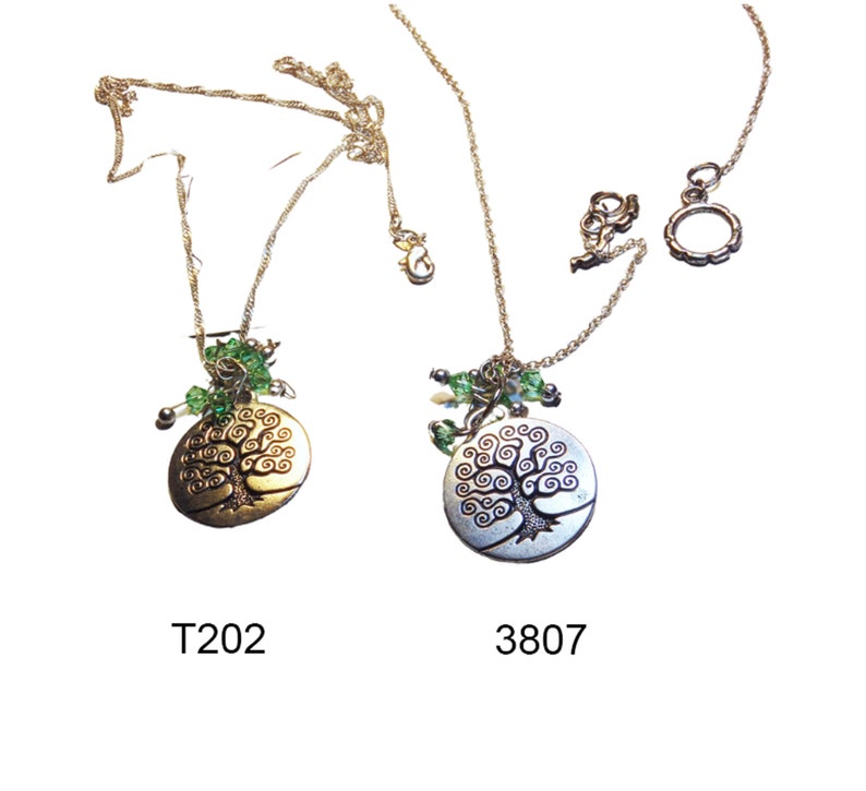 May include: Two necklaces featuring tree of life pendants. One pendant is gold-toned, the other silver-toned. Both have green bead accents and are on delicate silver chains. The necklaces are labelled T202 and 3807.