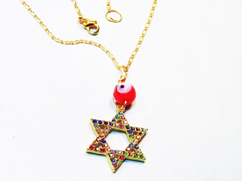 Gold necklace with a rainbow-colored rhinestone Star of David pendant and a red evil eye charm. The Star of David is intricately designed with small, sparkling rhinestones in various colors, including red, orange, yellow, green, blue, and purple. The red evil eye charm adds a pop of color and is believed to offer protection against negative energy. This necklace is a beautiful and meaningful piece of jewelry, perfect for everyday wear or special occasions.
