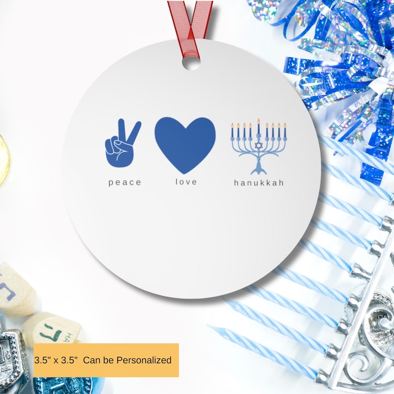 May include: A white Hanukkah ornament with blue graphics and a red ribbon. The ornament features the words 'peace', 'love', and 'hanukkah' with corresponding symbols: a peace sign, a heart, and a menorah. The ornament is 3.5' x 3.5' and can be personalized.