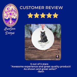 Op de afbeelding: Een witte ronde kerstversiering met een illustratie van een zwarte kat, de naam "FRITZY" en het jaar "2024". De versiering is versierd met een takje groen en een rood lint. De achtergrond bevat de tekst "CUSTOMER REVIEW".