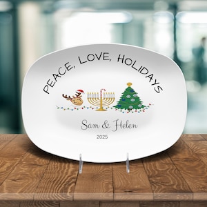 May include: White oval platter with the words "PEACE, LOVE, HOLIDAYS" in a curved arc. The platter features a reindeer wearing a Santa hat, a menorah, and a Christmas tree. The names "Sam & Helen" and the year "2025" are also printed on the platter.