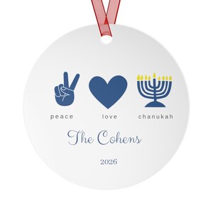 May include: A round white ceramic ornament with a red ribbon hanger. The design features a blue peace sign, a blue heart, and a blue menorah with yellow flames. Below are the words peace, love, chanukah, the name The Cohens, and the year 2026.