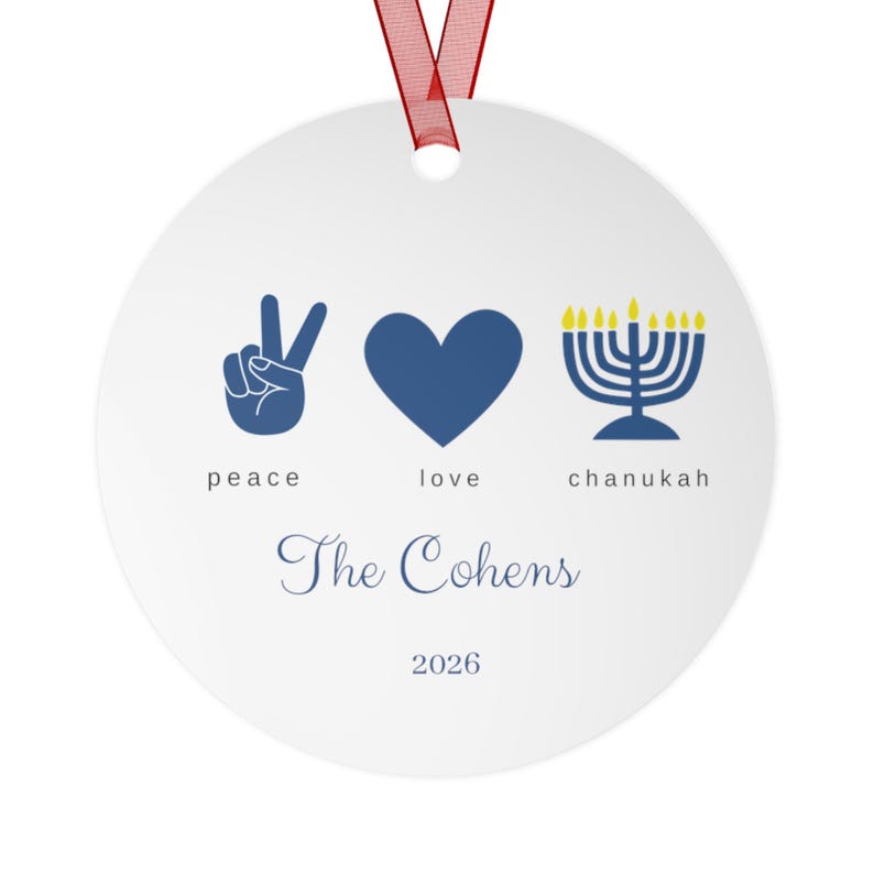 May include: A round white ceramic ornament with a red ribbon hanger. The design features a blue peace sign, a blue heart, and a blue menorah with yellow flames. Below are the words peace, love, chanukah, the name The Cohens, and the year 2026.