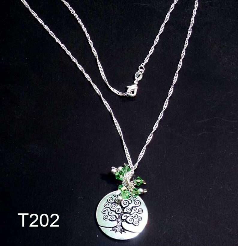 May include: A silver necklace with a tree of life pendant. The pendant is a pale green disc with a black tree design. The necklace has a fine chain and a clasp. Green beads are clustered above the pendant. The text "T202" is in the lower left corner of the image.