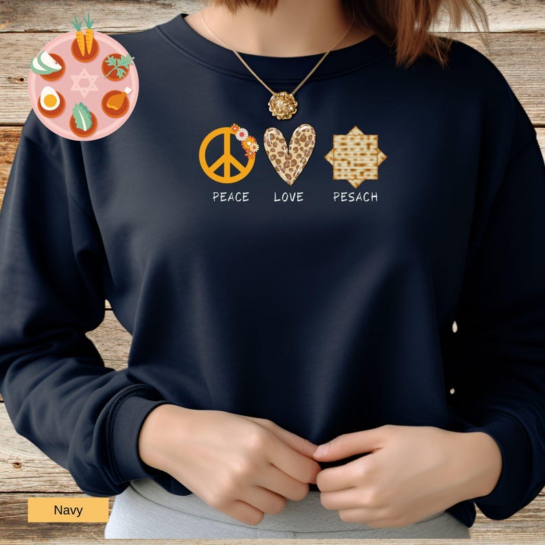 May include: A navy blue sweatshirt with a peace sign, heart, and matzah design. The peace sign is yellow with a floral design. The heart is leopard print. The matzah is a traditional Jewish bread. The text below the design reads 'Peace Love Pesach'.