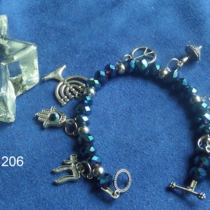 May include: A beaded bracelet with dark blue faceted beads and silver-tone charms, including a peace sign, a Hamsa hand, and a Torah scroll. A clear, star-shaped object is in the upper left corner. The number "206" is visible.