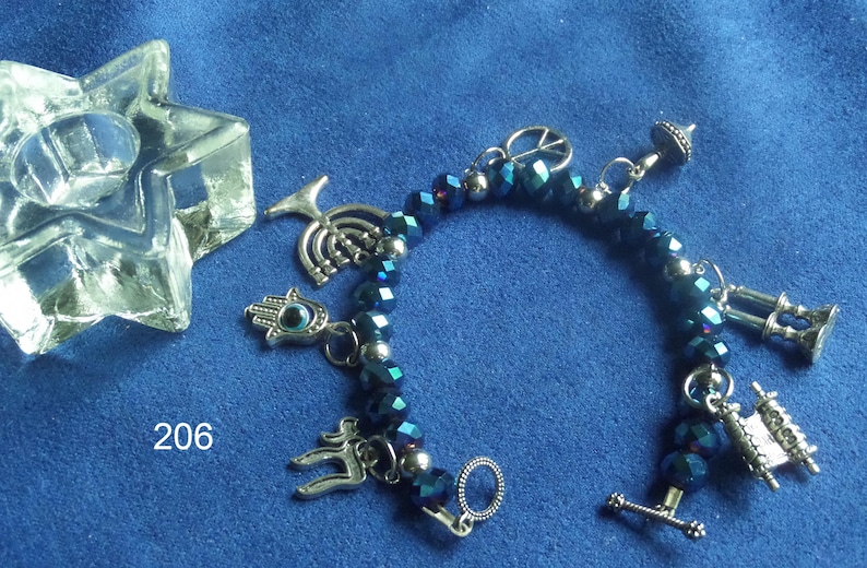 May include: A beaded bracelet with dark blue faceted beads and silver-tone charms, including a peace sign, a Hamsa hand, and a Torah scroll. A clear, star-shaped object is in the upper left corner. The number "206" is visible.