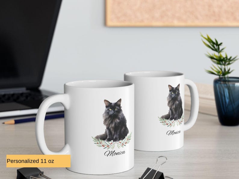 May include: Two white ceramic mugs with black handles. Each mug has a black cat illustration with a floral design and the name 'Monica' printed below. The mugs are on a light brown wooden surface.