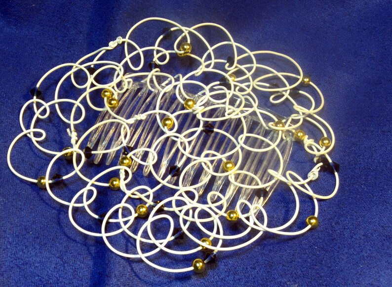 May include: A white wire hair comb with gold and black beads. The comb is decorated with a swirling pattern of wire.