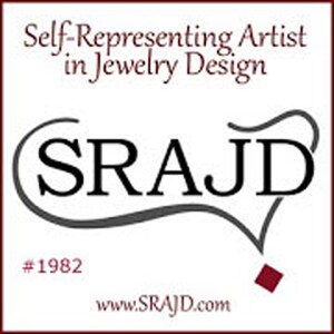May include: A square logo featuring the text Self-Representing Artist in Jewelry Design at the top, the acronym SRAJD in large black letters with a decorative flourish, the number #1982, and the website address www.SRAJD.com in dark red text.