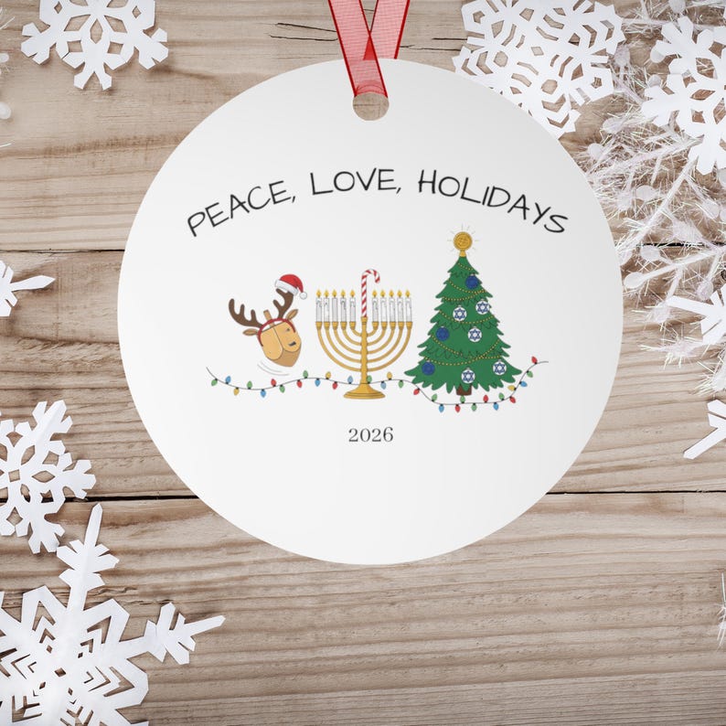 May include: A round white ceramic ornament with a red ribbon hanger. The text reads PEACE, LOVE, HOLIDAYS and 2026. Graphics include a reindeer wearing a Santa hat, a gold menorah with a candy cane, and a green Christmas tree with string lights.