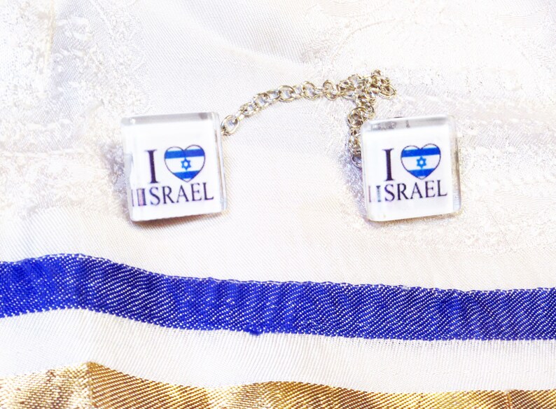 May include: Two square glass charms with a silver chain connecting them. Each charm has a white background with the text "I love Israel" and a blue and white heart with the Star of David inside.