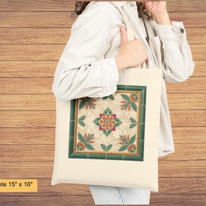 K&ouml;nnte beinhalten: Leinwand-Tragetasche, 38 cm x 41 cm, mit einem quadratischen Blumendesign und einem gr&uuml;nen Rand. Das Design umfasst die Farben Orange, Gr&uuml;n und Creme. Die Tasche besteht aus hellem Canvas-Material.