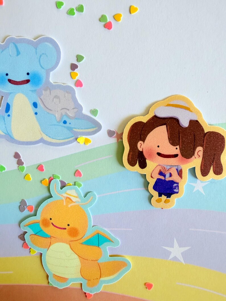 May include: A collection of colorful stickers featuring cartoon characters and heart-shaped confetti. The stickers include a blue creature, an orange dragon-like figure, and a girl with brown pigtails. The background has a pastel rainbow design.