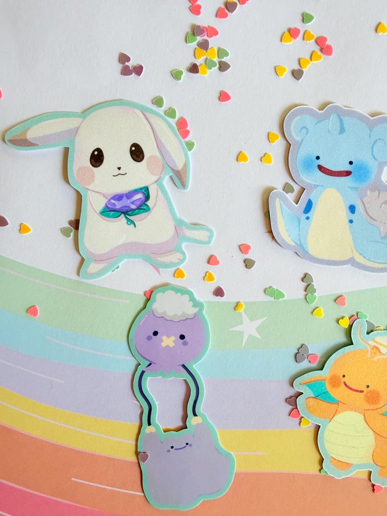 May include: A collection of colorful cartoon stickers featuring various creatures. The stickers include a white bunny holding a purple flower, a blue creature with a smiling face, and other whimsical designs. Scattered heart-shaped confetti adds a playful touch.