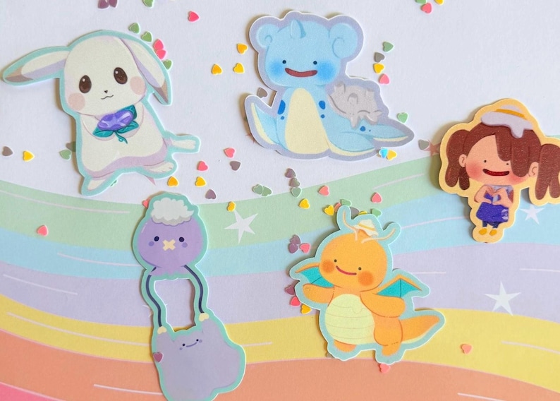 May include: A collection of colorful cartoon stickers featuring various cute characters. The stickers include a white bunny with a flower, a blue sea creature, a girl in a dress, a purple creature, and an orange dragon. The background is a pastel rainbow.