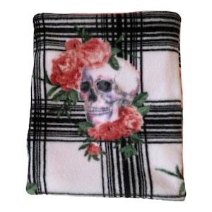 May include: White fleece throw blanket with a black and white plaid pattern. A skull with red and pink roses is printed on the blanket.