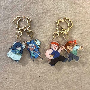 Peut inclure: Quatre porte-clés en acrylique avec des fermoirs dorés. Les porte-clés présentent des personnages de pirates de dessins animés dans diverses poses. L'un des porte-clés représente un personnage féminin en robe bleue.