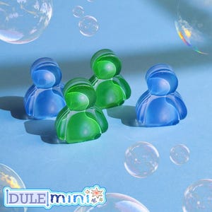 K&ouml;nnte beinhalten: Vier durchscheinende Figuren in Blau und Gr&uuml;n auf hellblauem Hintergrund mit schwebenden Blasen. Die Figuren haben eine abgerundete Form, die einer Person &auml;hnelt. Das Bild enth&auml;lt auch den Text "DULE mini".