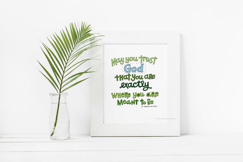 May include: A white framed print with a green and blue inspirational quote that reads "May you trust God that you are exactly where you are meant to be." The quote is written in a whimsical font.