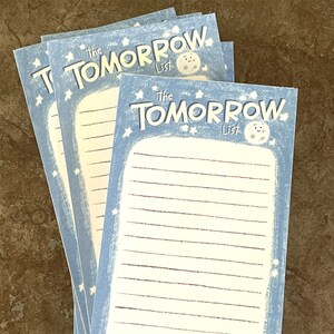 May include: A stack of blue and white to-do list pads with the text "The Tomorrow List" and a cartoon moon with a face.